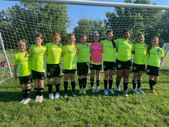 QC Elite U11 girls team in their lime kit, lined up together in front of the goal.